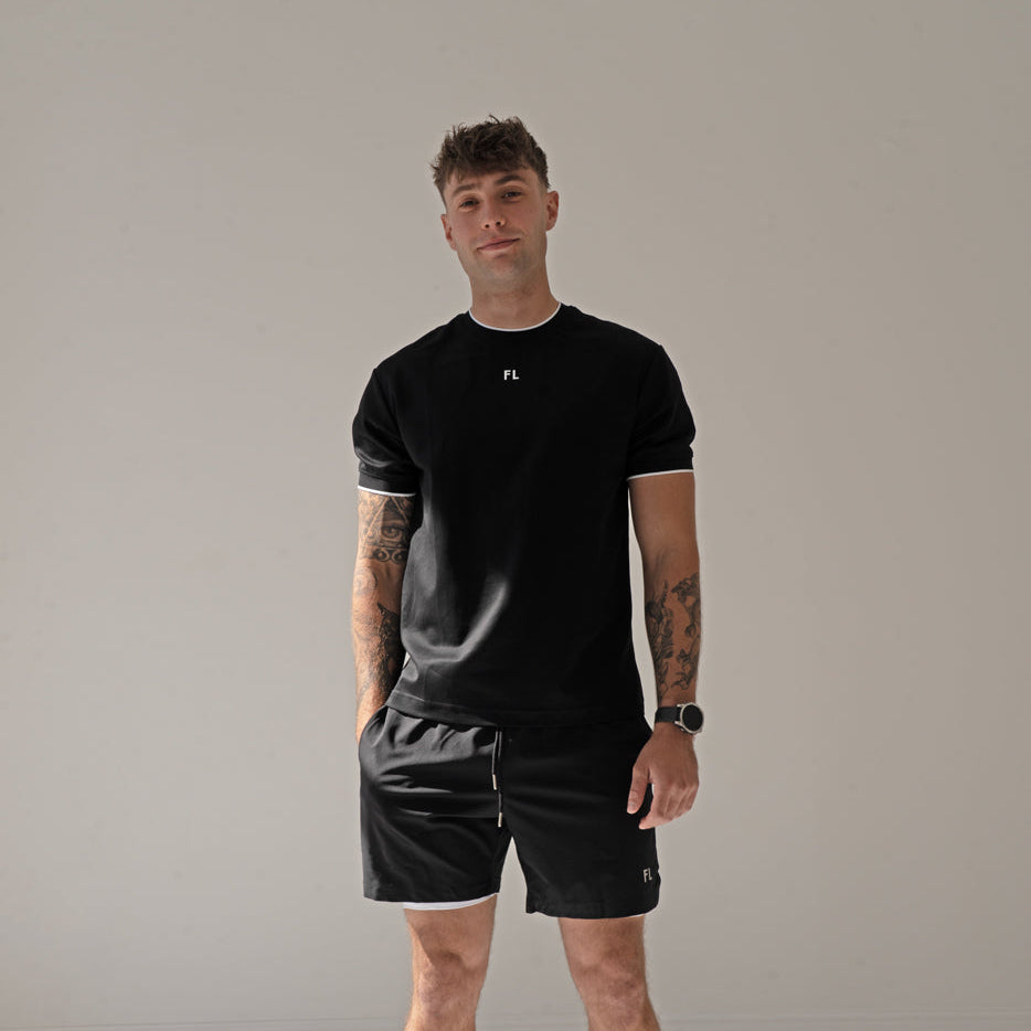 Man wearing a black padel t-shirt and shorts standing against a plain background