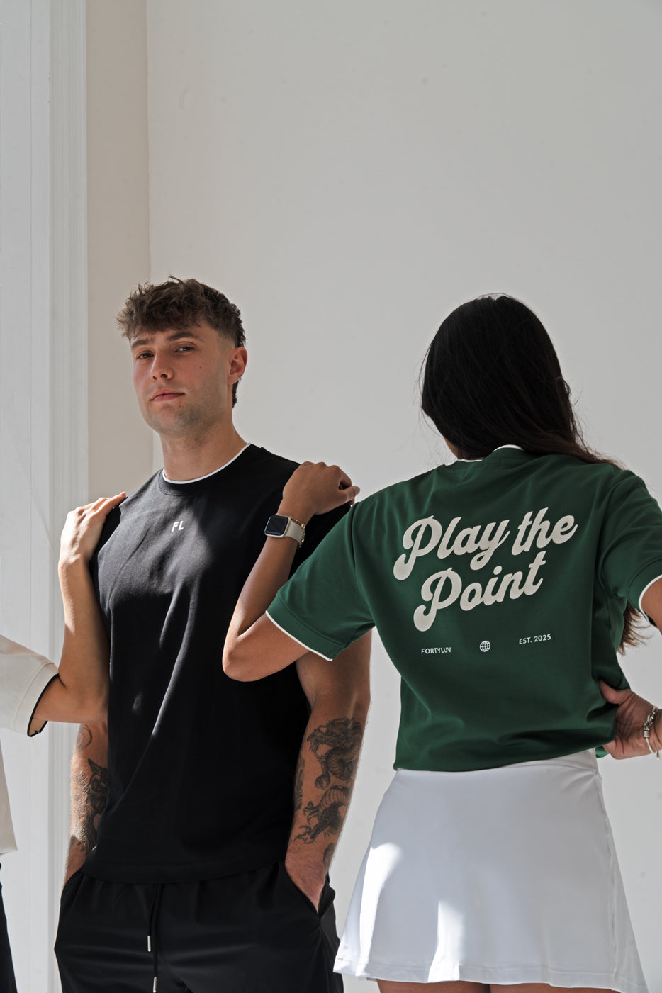 Two people standing close together, one wearing a black t-shirt and the other a green t-shirt with 'Play the Point' text.