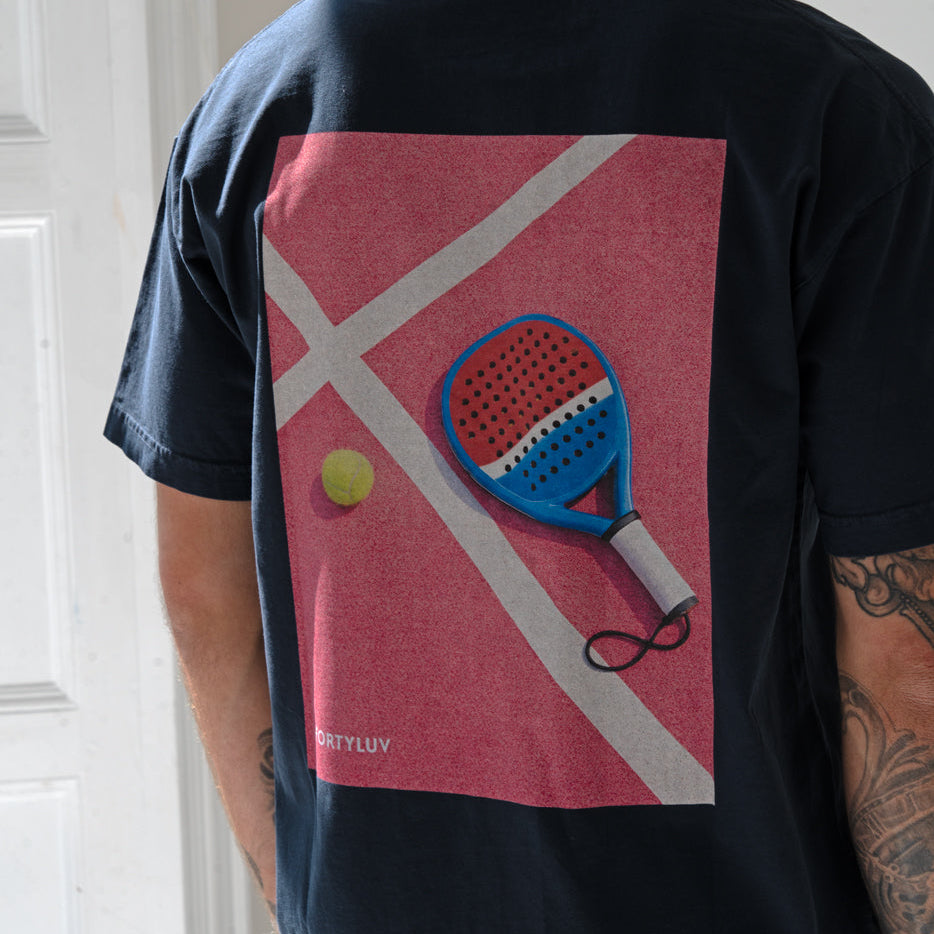 Person wearing a black t-shirt with a padel racket and ball design on a red background.